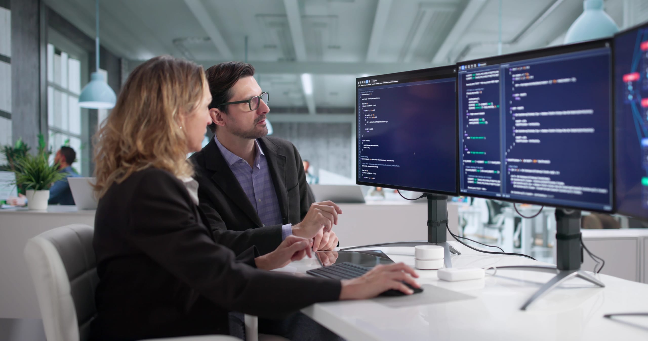 Two people discussing code on a computer screen in an office.