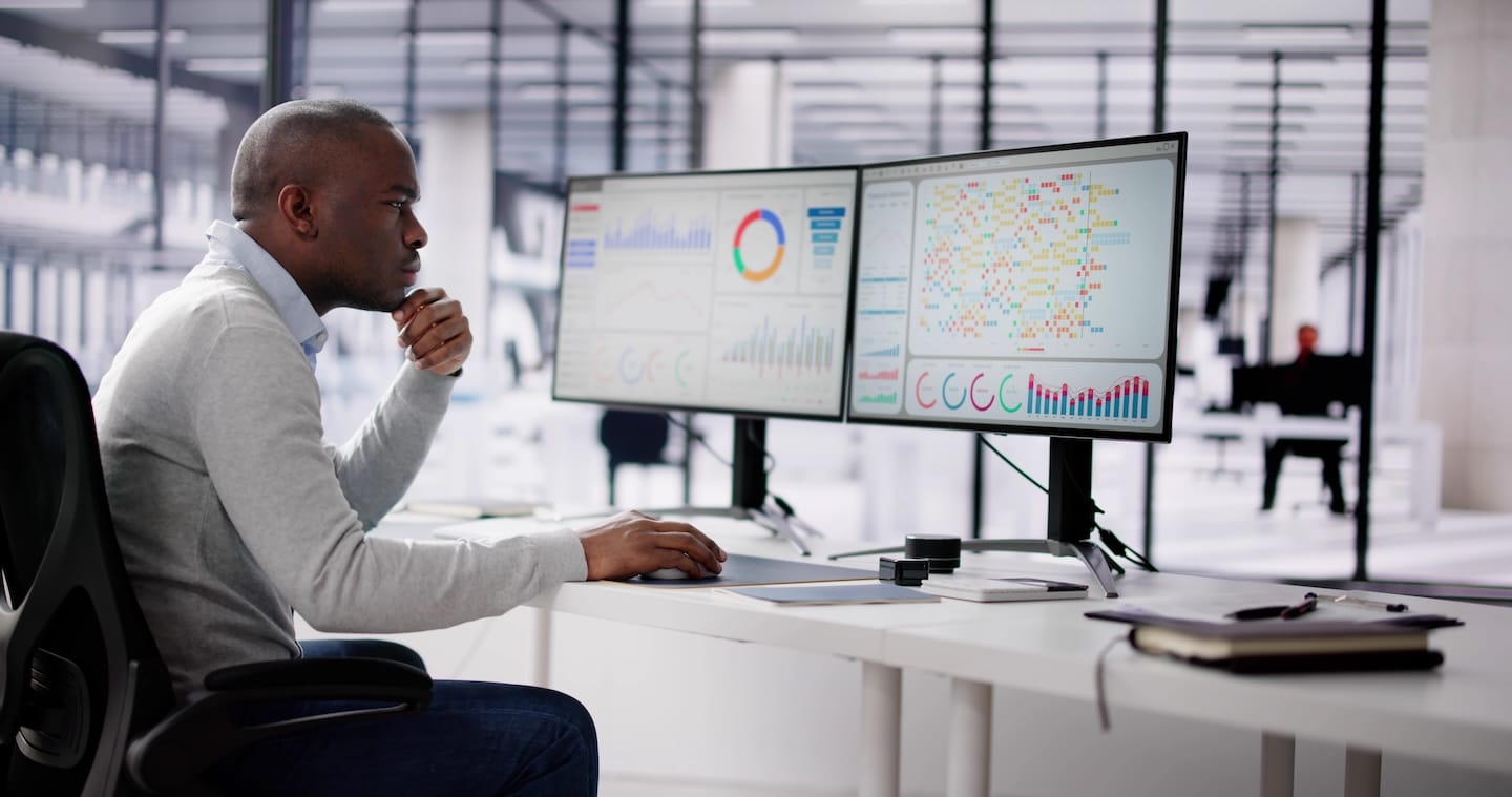 Person analyzing data on dual monitors in a modern office.