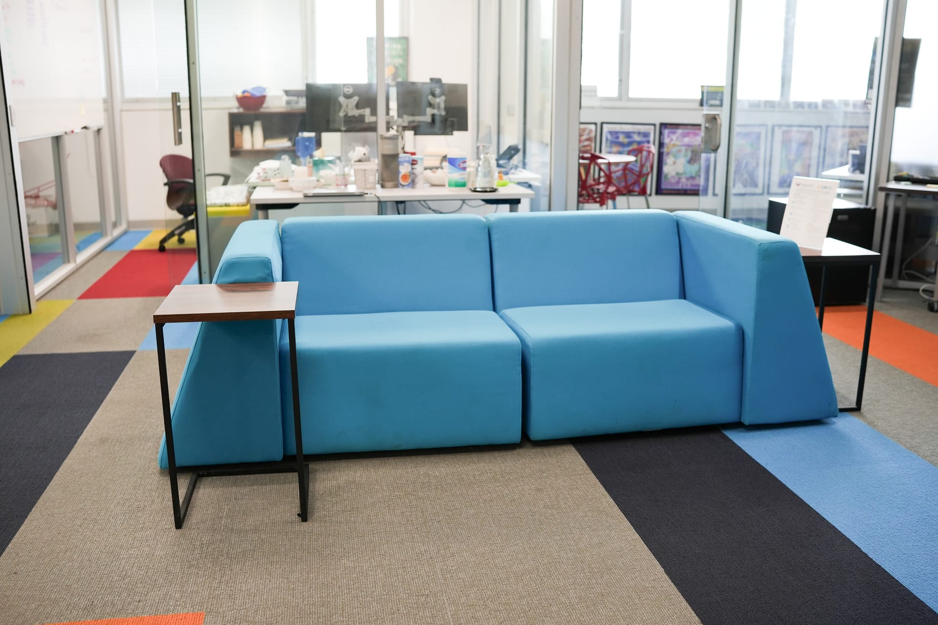 A blue sofa with side tables in an office lounge area with colorful carpet.