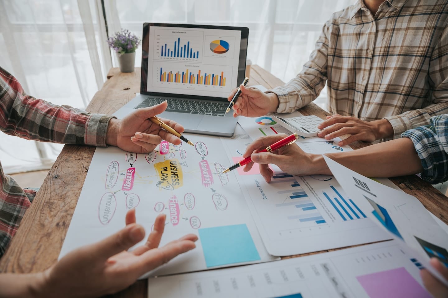 People discussing and pointing at business charts on a wooden table