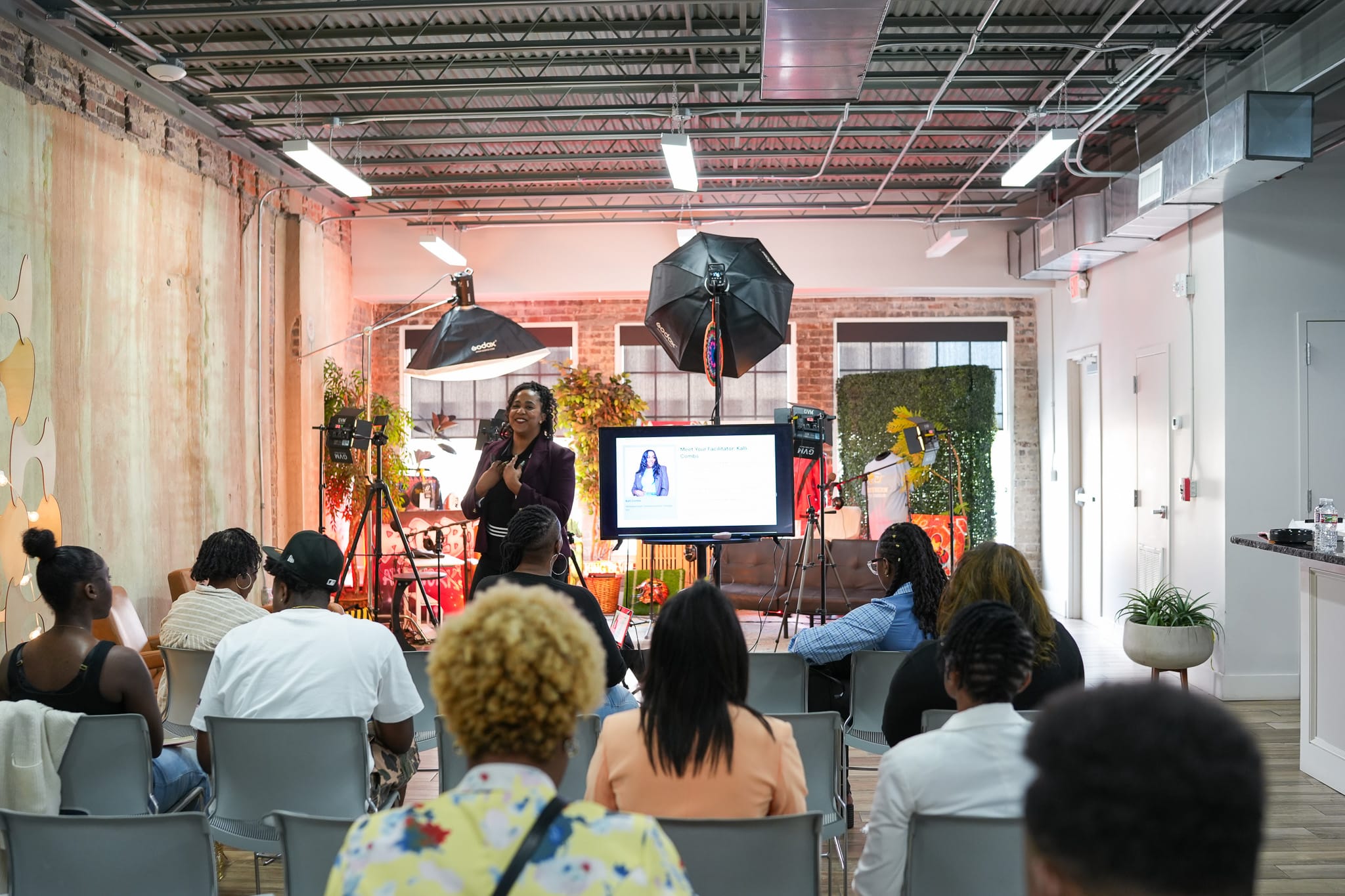 A speaker addresses an audience in a modern, well-lit venue with presentation equipment