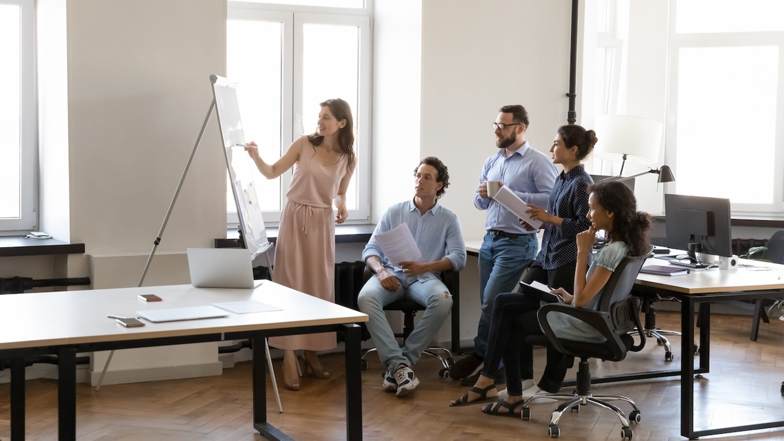 Five colleagues discussing a presentation in a modern office setting.
