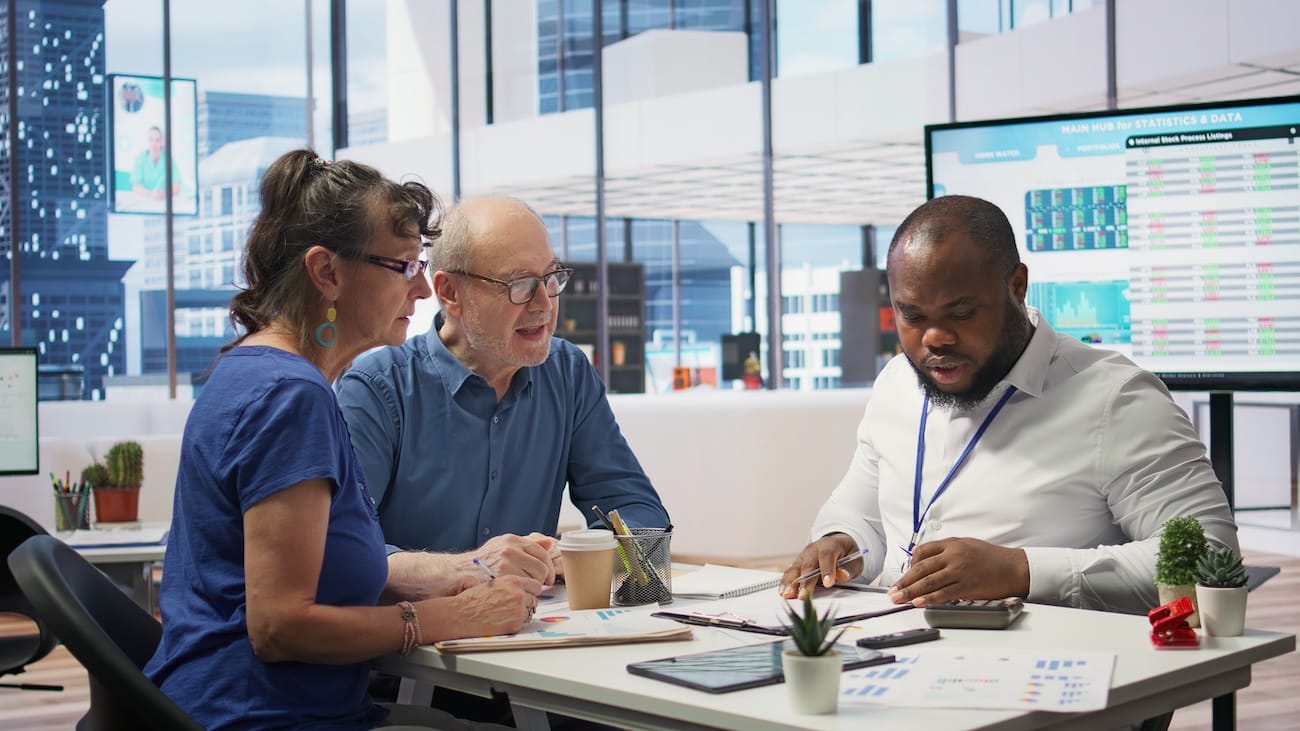 Three professionals having a discussion at a table in a modern office.