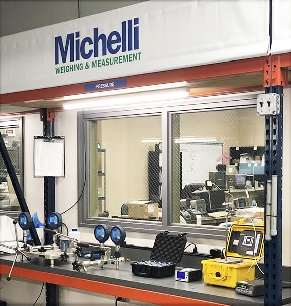 Michelli calibration technician at a pressure calibration workstation with gauges and reference standards
