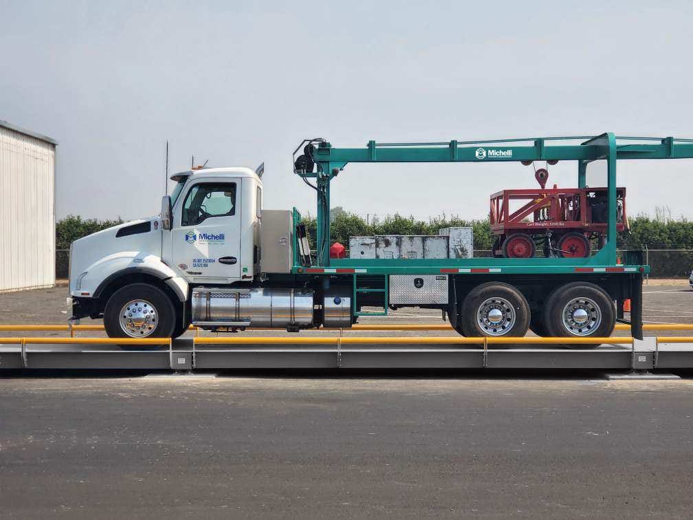 A white truck with a green crane parked on an industrial scale