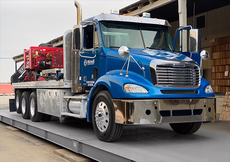 A blue heavy-duty truck on a platform scale with a red machinery section.