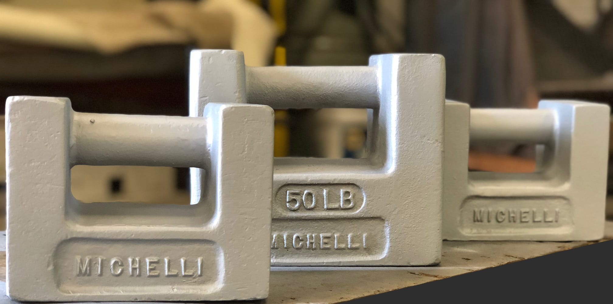 Three stacked 50 LB Michelli calibration weights on a workshop surface