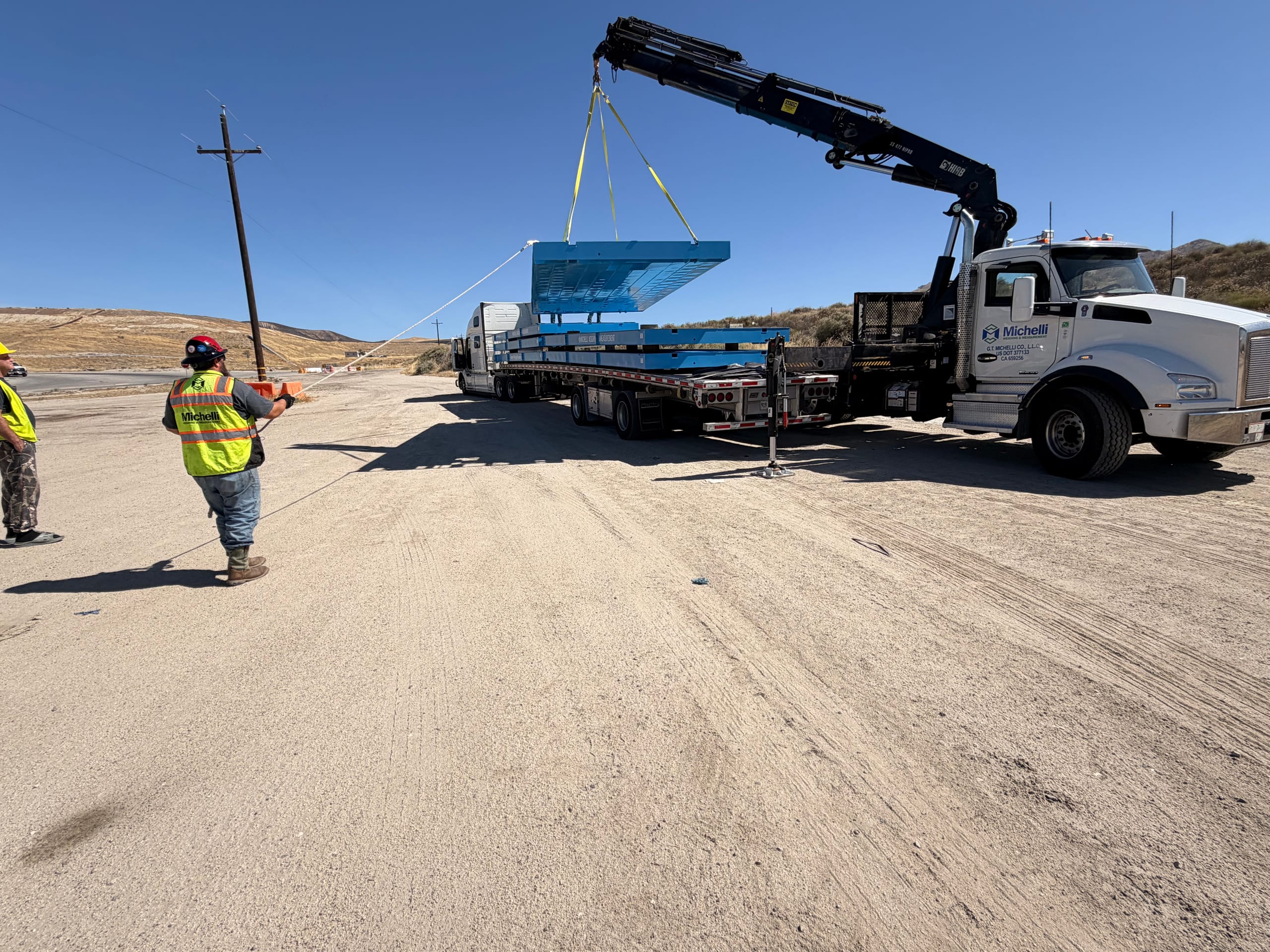 Construction workers guiding a suspended structure with a crane on a sandy site