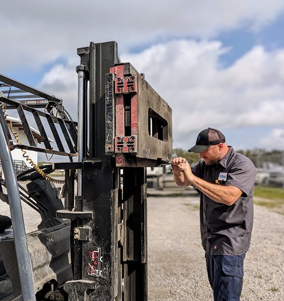 Mechanic repairing forklift attachment outdoors