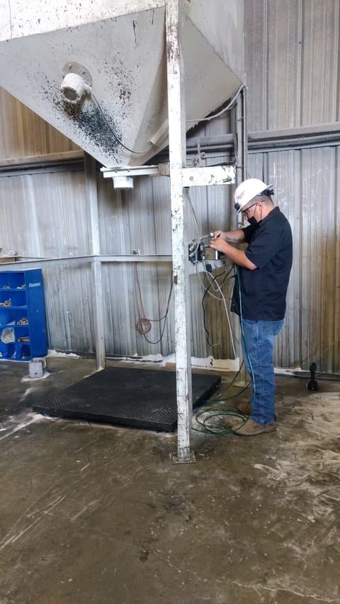 Worker repairing a floor scale under a hopper in an industrial facility