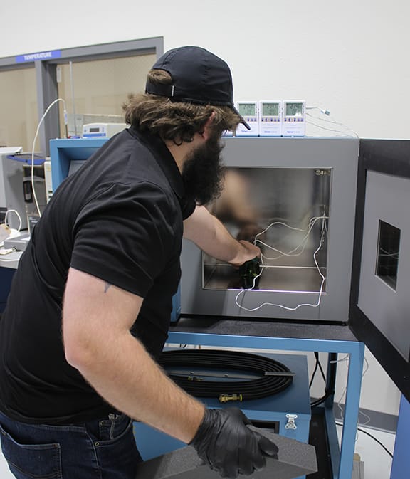A bearded technician inserts an item into a test chamber in a laboratory.