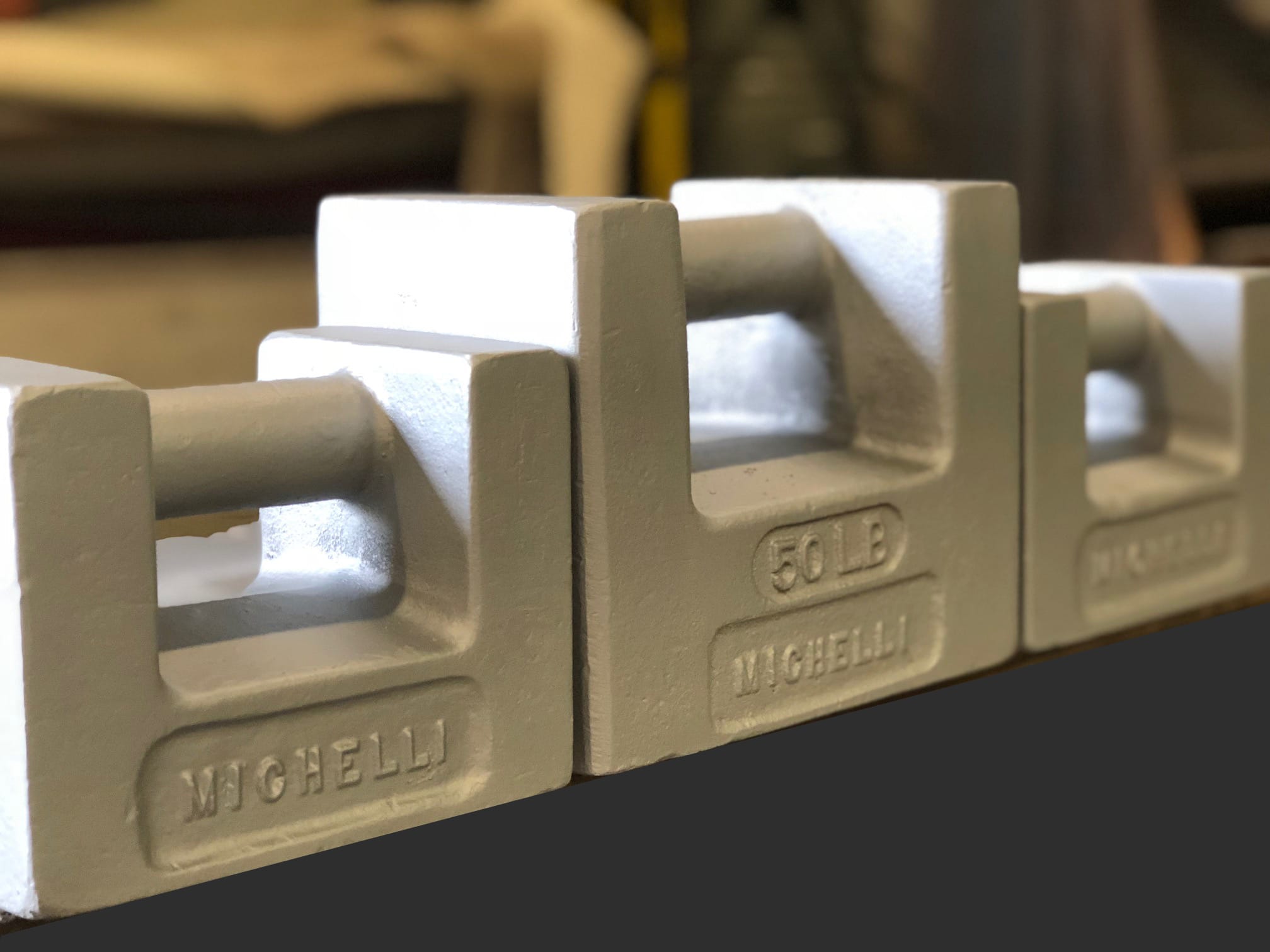 Three gray industrial weight blocks with handles, labeled Michelli and 50 LB.