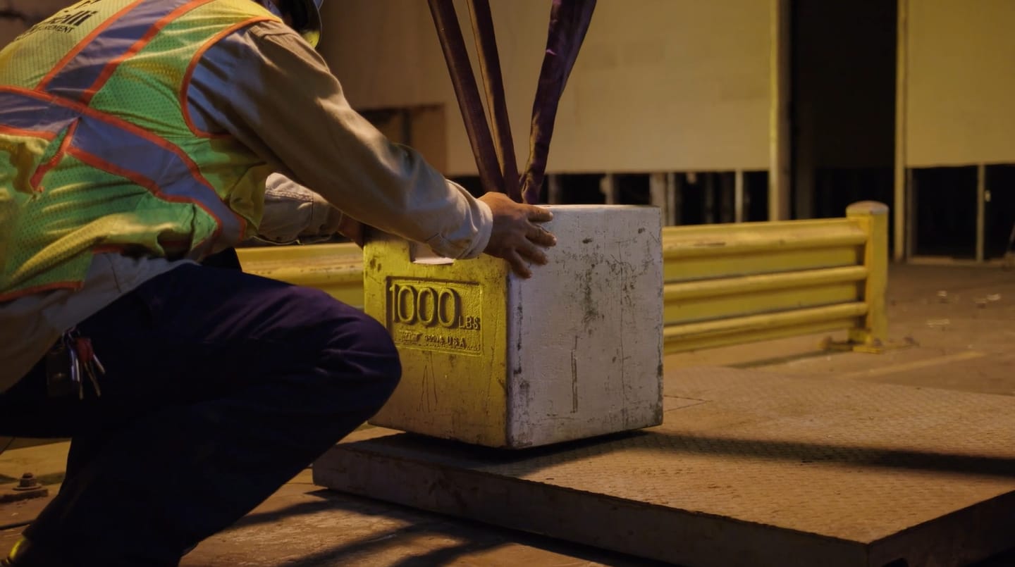 A person kneels to adjust a 1000 lbs test weight on a metal platform.
