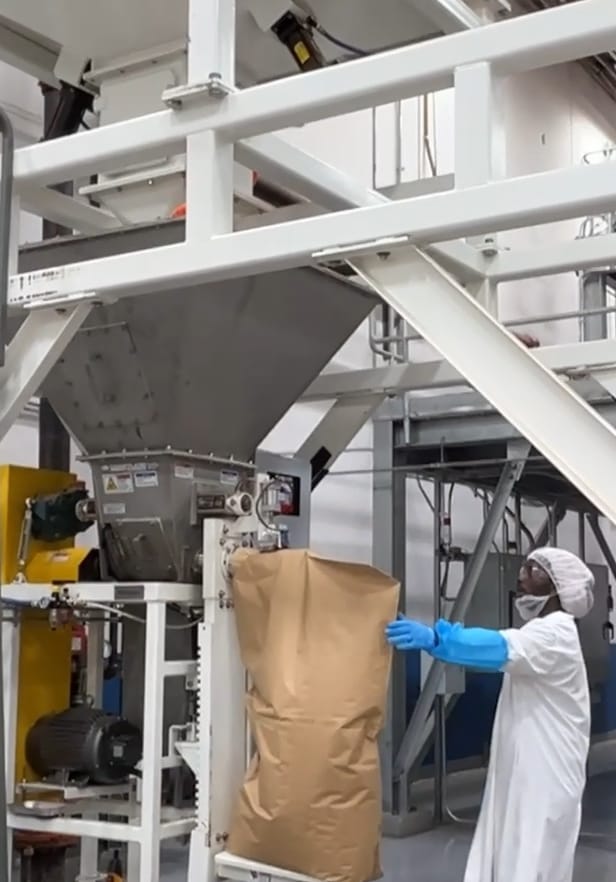A worker packages tea into a brown paper bag using the quality control weighing system