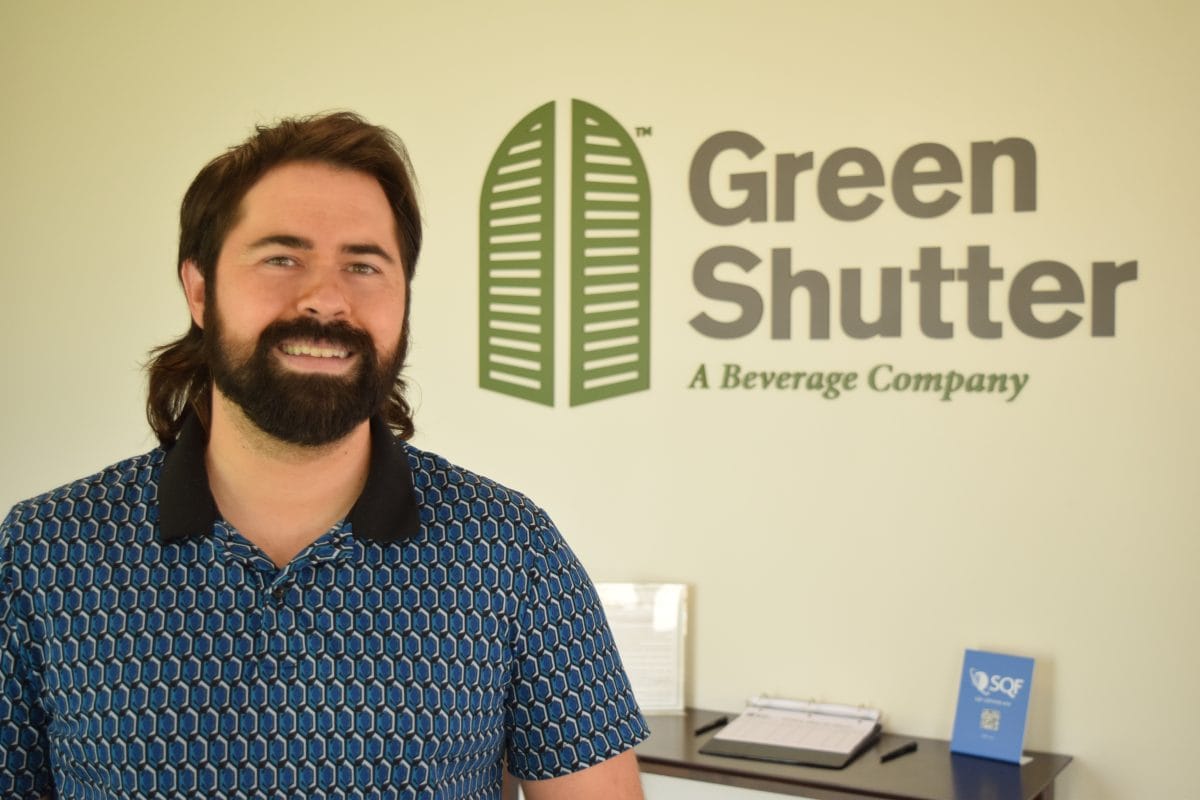 Lenny Zichichi, COO, Green Shutter Tea smiles in front of the Green Shutter Tea sign