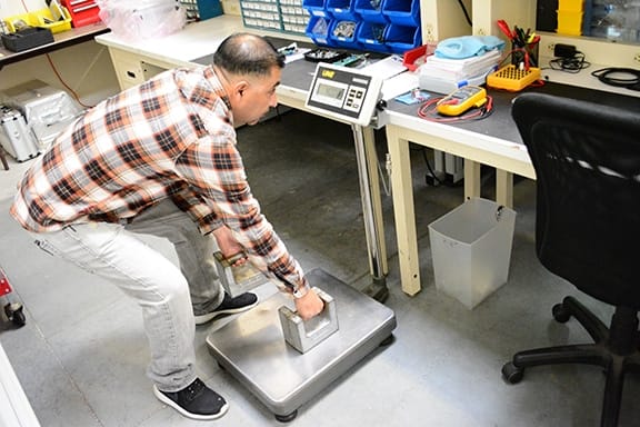 A scale technician uses test weights to calibrate a scale during routine maintenance