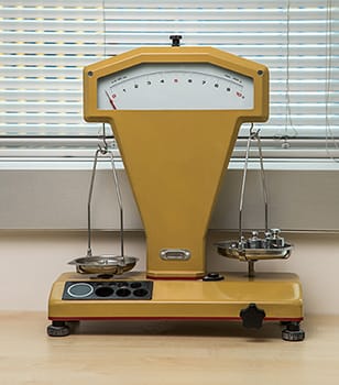 Yellow laboratory balance with calibration test weights placed on the weighing plate