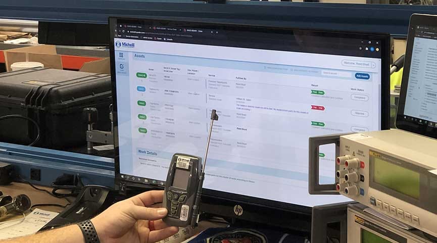 Laptop displaying the Michelli TRAC 2.0 asset management portal with calibration records in a lab setting