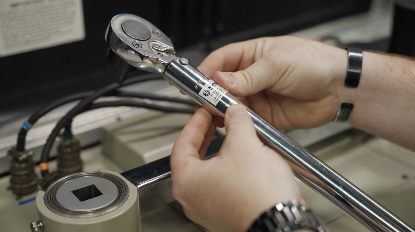 Hands adjusting a metal torque wrench near machinery.