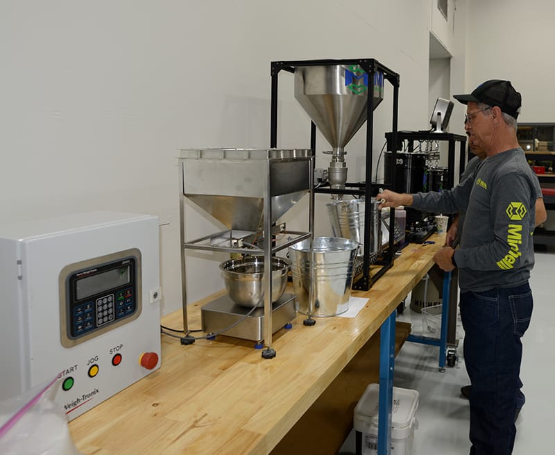 Man operating an industrial bulk weighing machine with digital control panel in a workshop