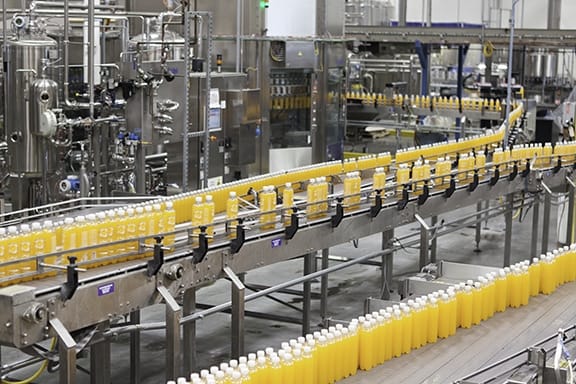 Rows of yellow juice bottles moving along a conveyor belt in a factory bottling line