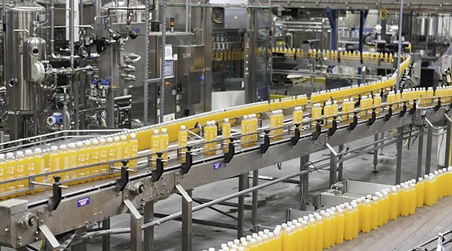 Rows of yellow juice bottles moving along a conveyor belt in a factory bottling line
