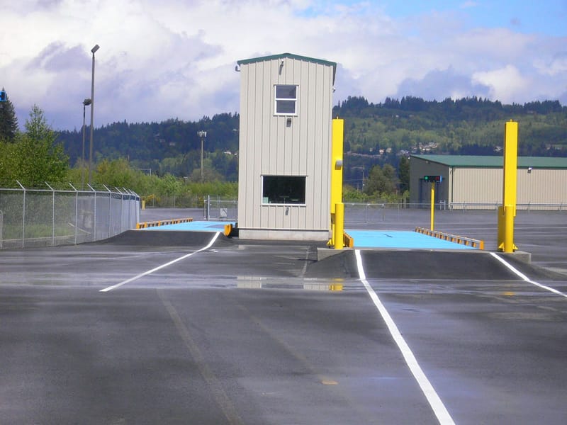 Vehicle inspection station with scale house building between two yellow columns on a ramp, mountains in background