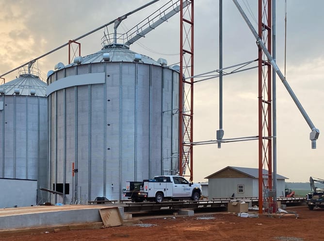 Utility truck parked in front of large grain silos at an agricultural and commodity handling site