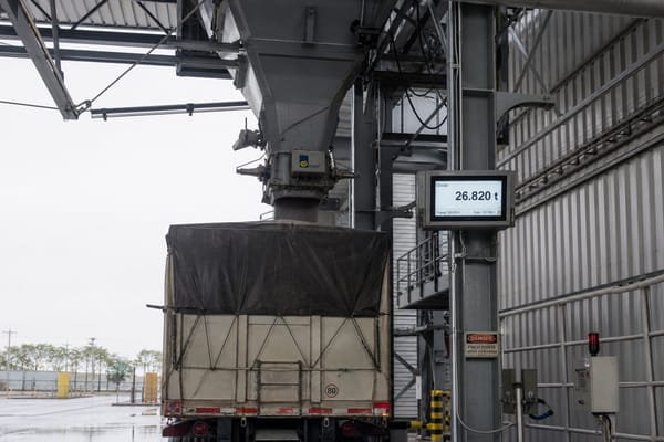 Bulk material discharge chute filling a container at an industrial loadout station with a weight indicator display