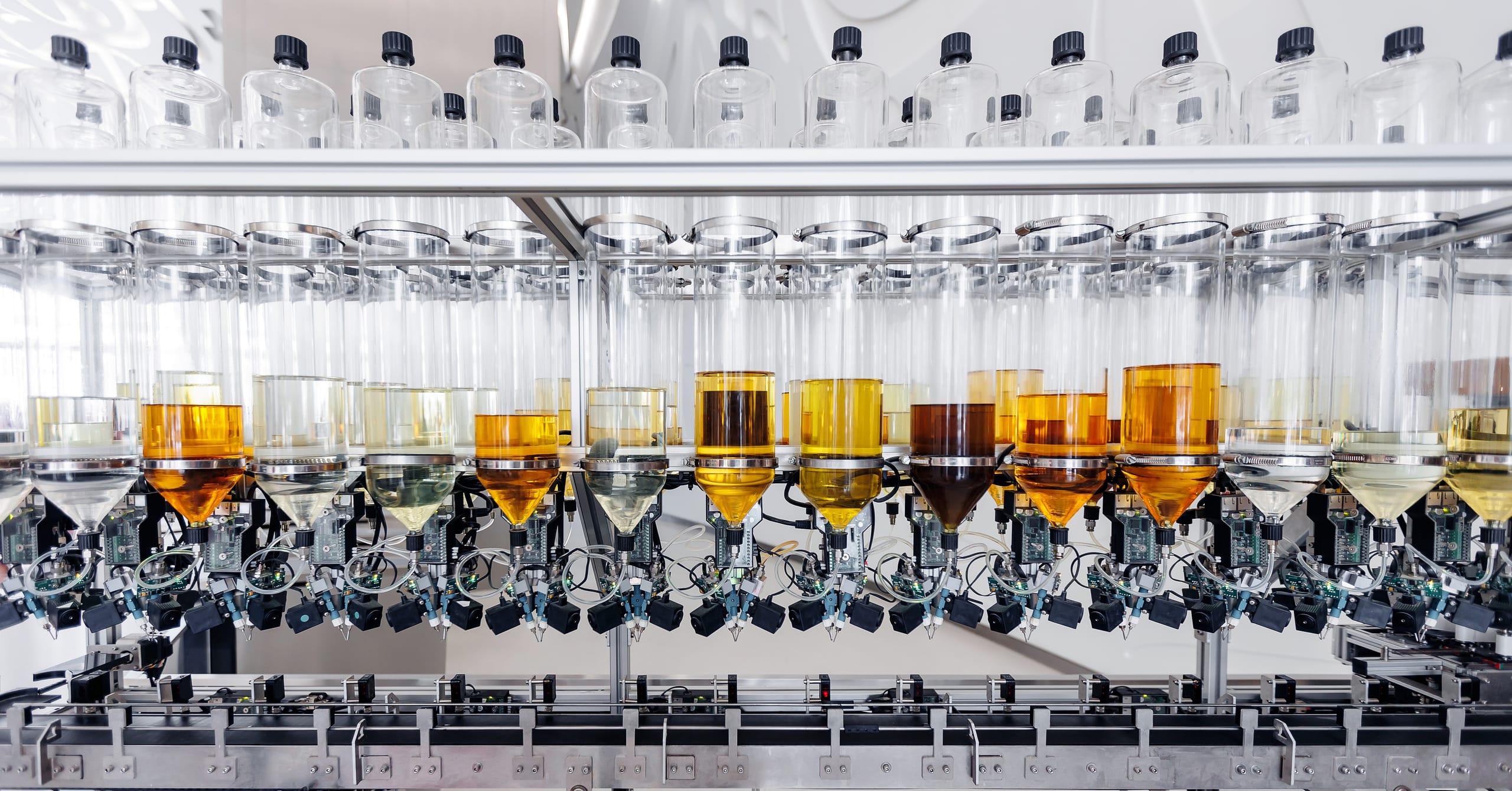 A row of transparent containers filled with various liquids in an automated lab dispensing system