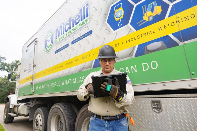 Michelli field service technician with tablet standing beside a branded service truck at an industrial facility
