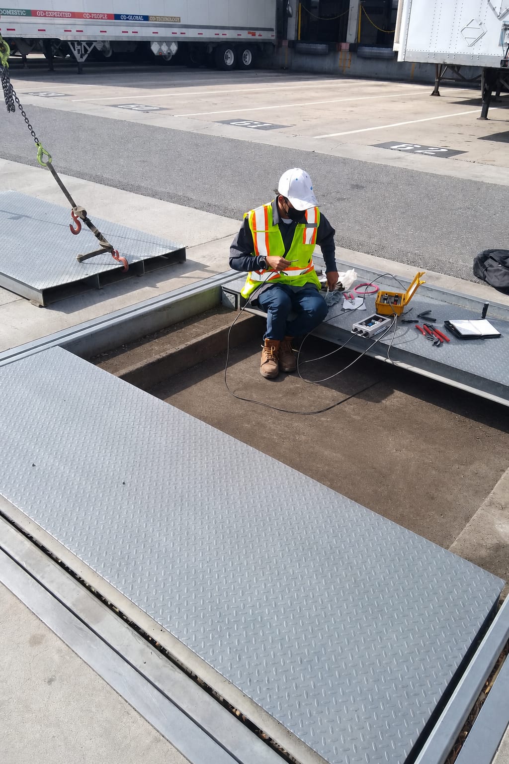 A technician in a safety vest inspects a truck scale at a loading dock