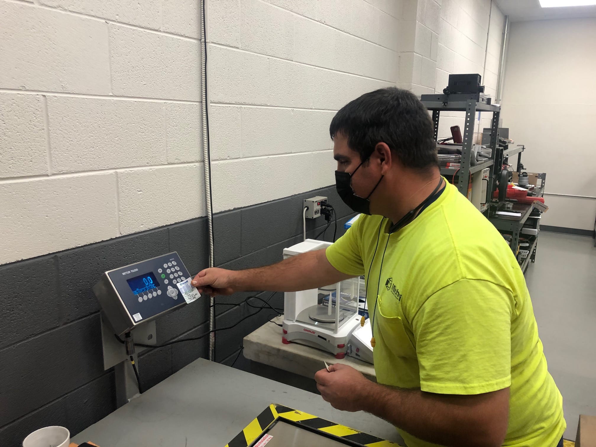 A person in a yellow shirt uses an electronic scale in a lab