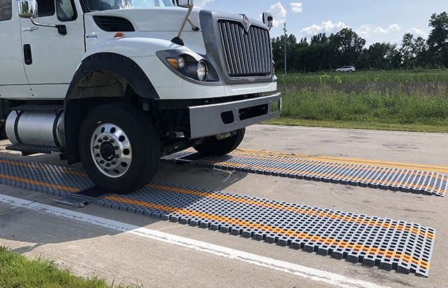 A truck parked on orange and gray portable weighing scales on a road.