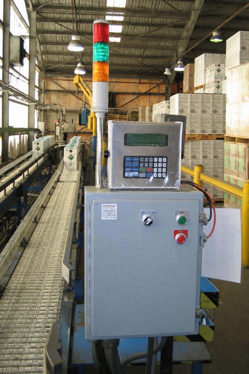 Industrial control panel with signal tower next to a conveyor belt in a warehouse facility