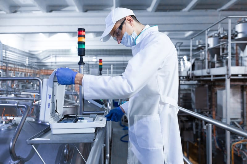 Technician in protective gear operating industrial equipment with indicator lights in a manufacturing facility