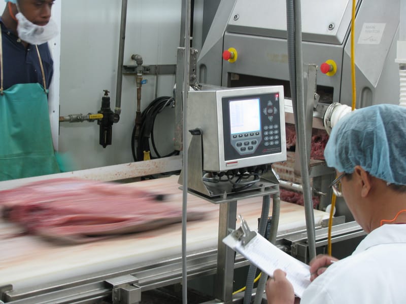Workers monitoring operations at a conveyor belt with a digital control panel in a meat processing plant