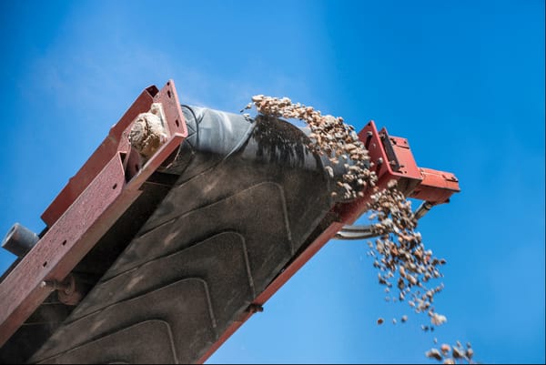 Conveyor belt unloading rocks against a clear blue sky in a mining or construction operation