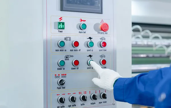 Gloved operator pressing a button on an industrial machine control panel for automated shutdown control