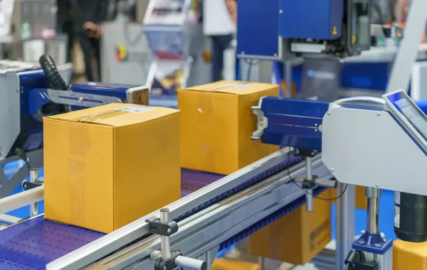 Cardboard boxes on an automated packaging conveyor belt with labeling and production reporting equipment