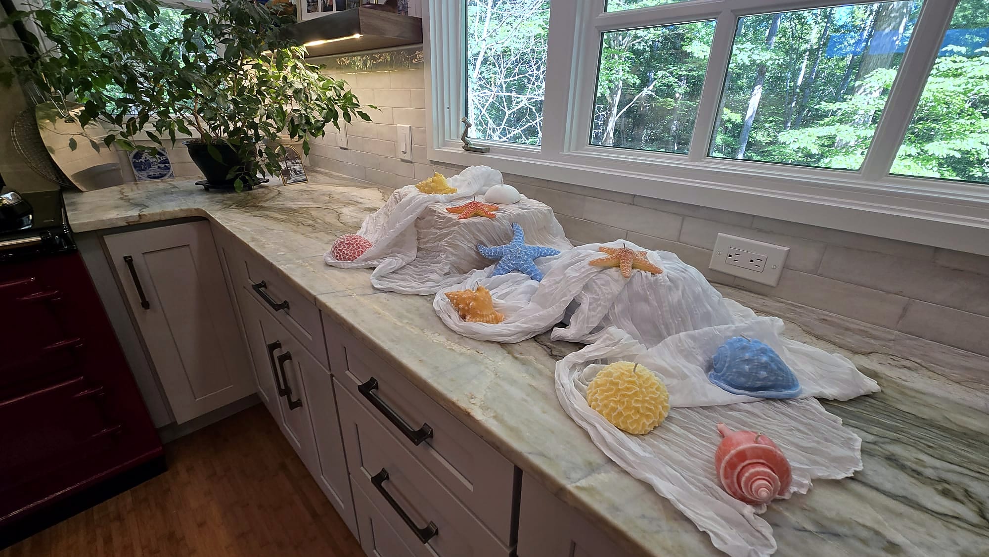 Handmade blue, pink, yellow, orange, and white ocean-form candles displayed on draped fabric over a marble counter.