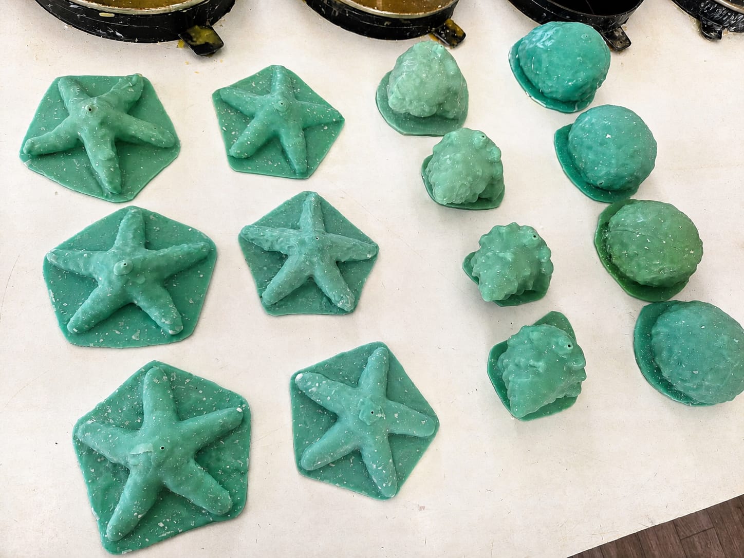 Green silicone starfish, shell, and coral candle molds arranged on a Candle Hut Barbados workshop table.