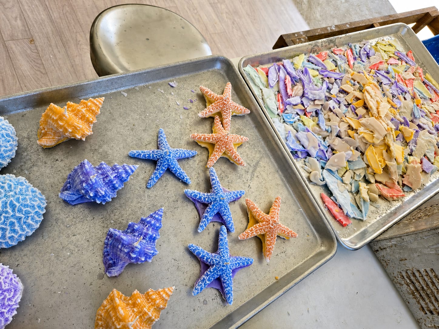 Colorful starfish, shell, and coral candles on a metal tray beside collected reusable wax offcuts.