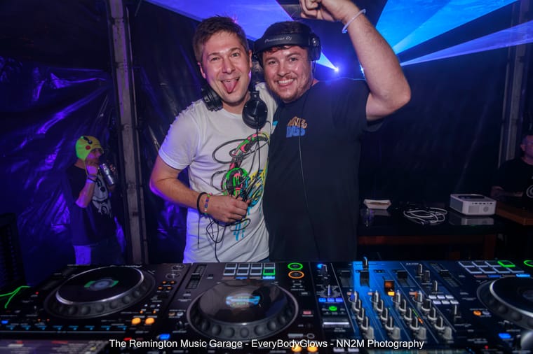 Two DJs with headphones smiling behind DJ equipment