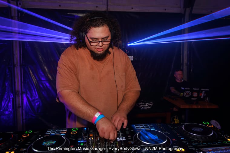 A DJ mixing on a console with laser lights overhead