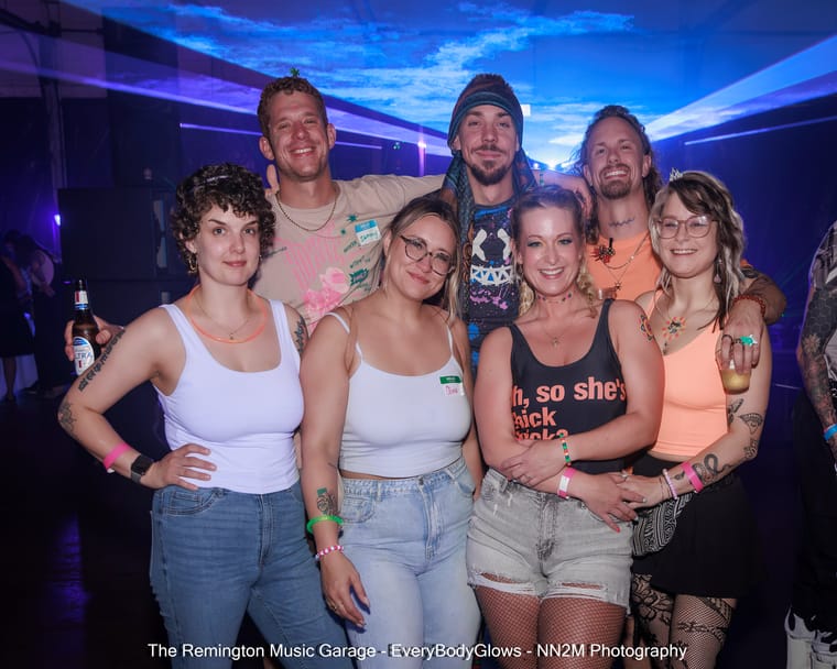 A group of seven people posing together at a nightclub with colorful lighting