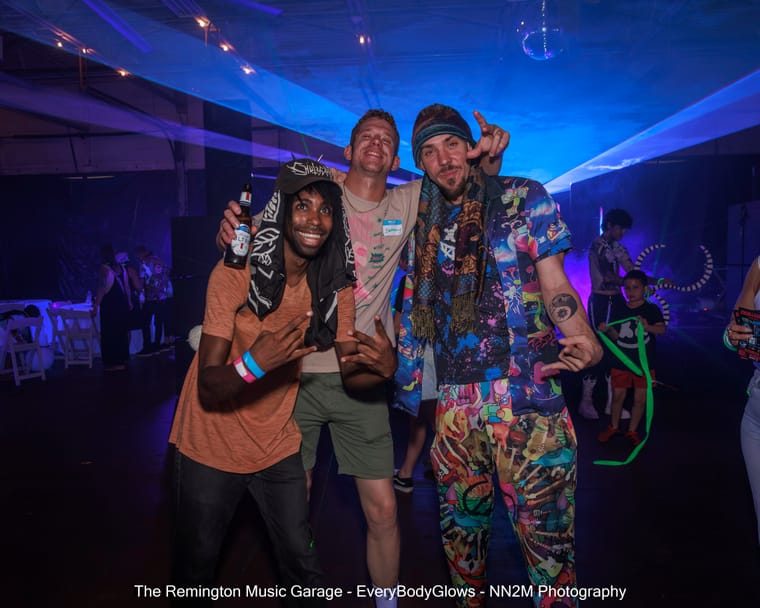 Three men posing and smiling at a lively party under vibrant lighting