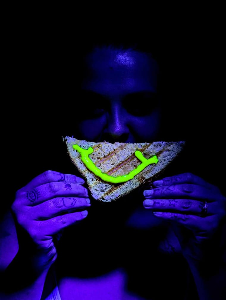 Person holding a grilled sandwich with a neon smiley face drawn on it