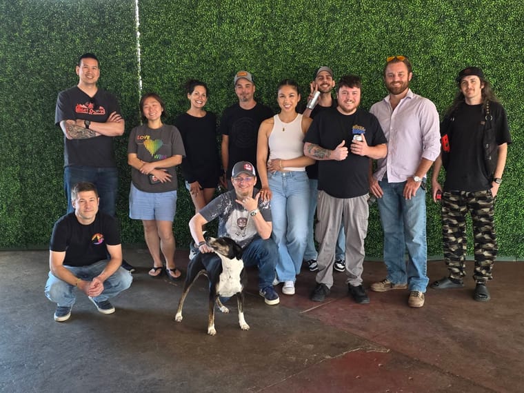 A group of eleven people and a dog pose in front of a green wall