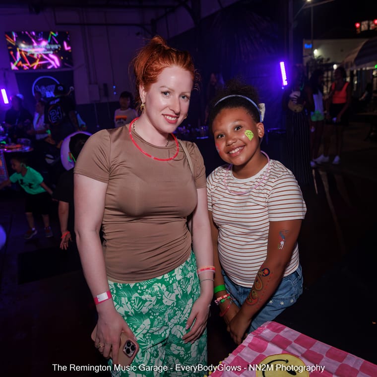 Two smiling individuals at a glow-themed event with neon lights